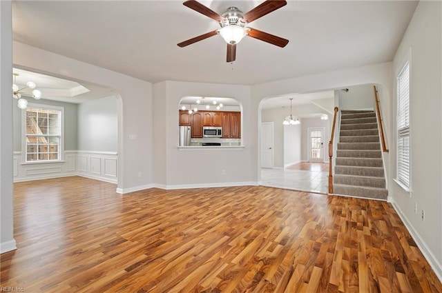 unfurnished living room with a wealth of natural light, stairway, arched walkways, and light wood-style flooring