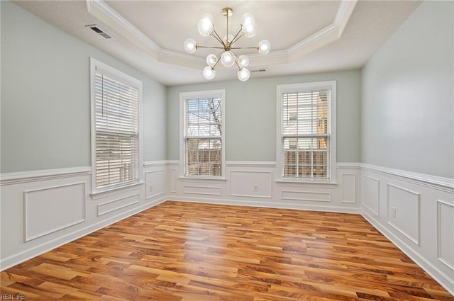 unfurnished dining area featuring visible vents, a notable chandelier, a tray ceiling, light wood-style floors, and crown molding