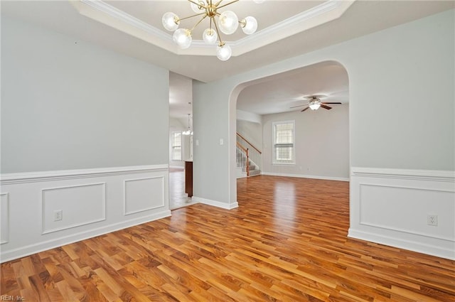 spare room with light wood finished floors, arched walkways, ornamental molding, stairs, and a raised ceiling