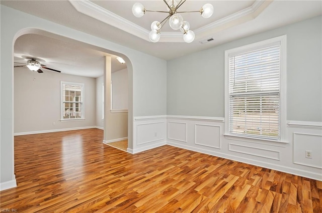 unfurnished room featuring visible vents, light wood-style flooring, arched walkways, ornamental molding, and a raised ceiling