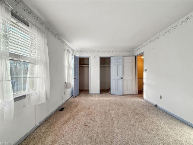 unfurnished bedroom featuring carpet flooring, visible vents, baseboards, and multiple closets