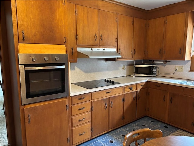 kitchen featuring under cabinet range hood, stainless steel appliances, brown cabinets, and light countertops