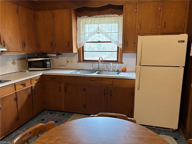 kitchen featuring freestanding refrigerator, a sink, decorative backsplash, light countertops, and stainless steel microwave