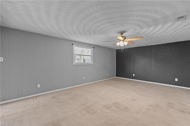 carpeted spare room with visible vents, a ceiling fan, a textured ceiling, brick wall, and baseboards