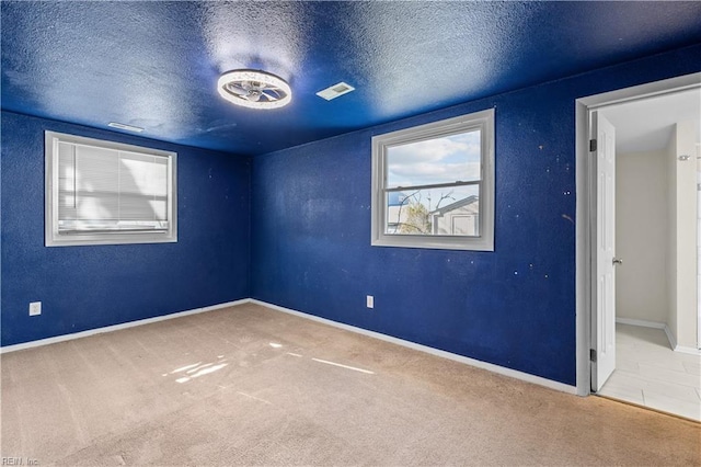 empty room with baseboards, visible vents, carpet floors, and a textured ceiling