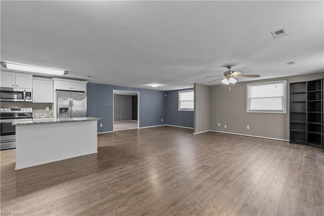 unfurnished living room with ceiling fan, visible vents, baseboards, and dark wood finished floors