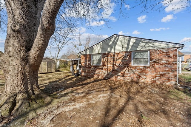 view of side of home featuring an outdoor structure, driveway, brick siding, and a shed