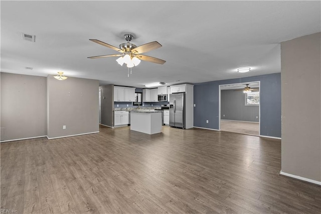 unfurnished living room featuring a ceiling fan, visible vents, dark wood-style flooring, and baseboards