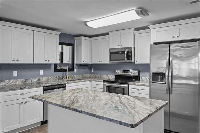 kitchen featuring a center island, light stone counters, stainless steel appliances, white cabinetry, and a sink