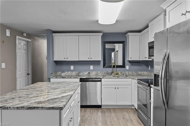 kitchen with a kitchen island, light wood-style flooring, appliances with stainless steel finishes, white cabinetry, and a sink