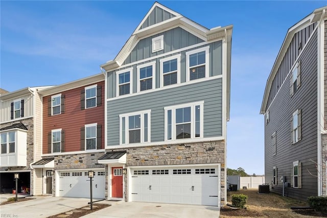 townhome / multi-family property with driveway, stone siding, central AC, board and batten siding, and a garage