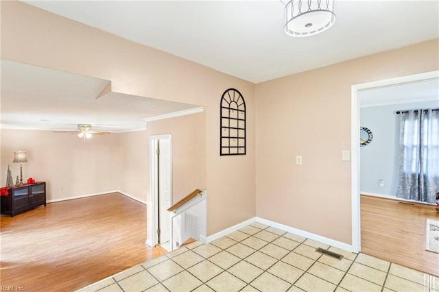 empty room featuring light wood finished floors, visible vents, baseboards, ornamental molding, and a ceiling fan