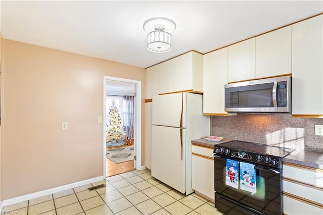 kitchen with electric range, stainless steel microwave, backsplash, freestanding refrigerator, and light tile patterned floors