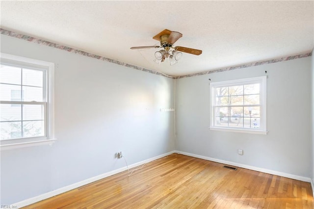 empty room featuring light wood finished floors, baseboards, visible vents, and a wealth of natural light