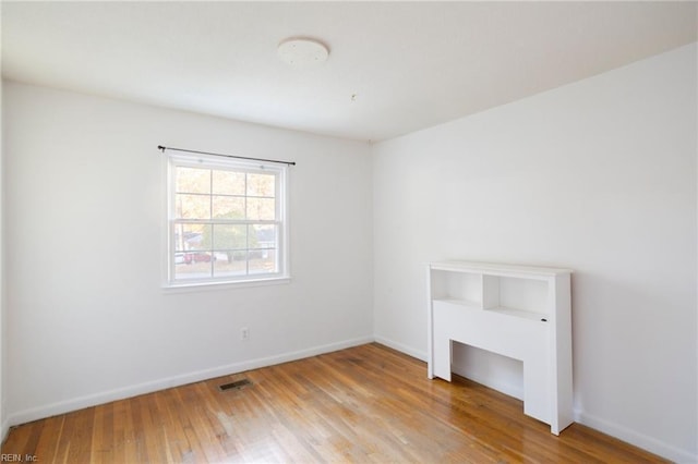 empty room featuring wood finished floors, visible vents, and baseboards