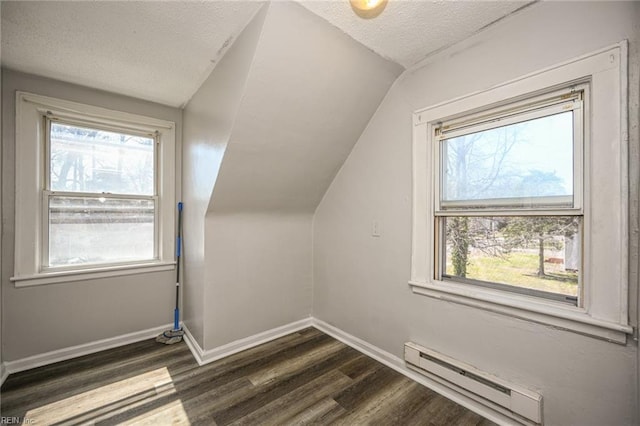 additional living space featuring a baseboard heating unit, baseboards, a wealth of natural light, dark wood-style floors, and a textured ceiling