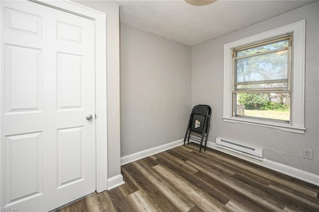 unfurnished room with a baseboard heating unit, dark wood-style floors, baseboards, and a textured ceiling