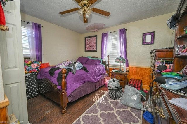 bedroom with wooden walls, a ceiling fan, wood finished floors, a wainscoted wall, and a textured ceiling