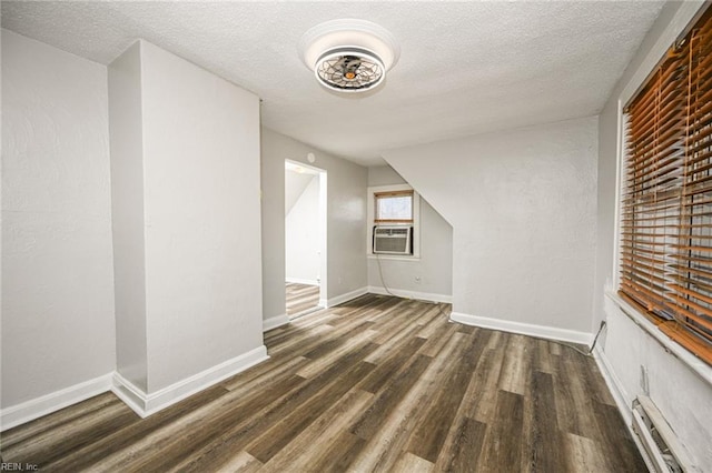 additional living space with baseboards, a textured ceiling, and wood finished floors