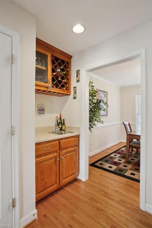 bar with baseboards, recessed lighting, a sink, a bar, and light wood-style floors