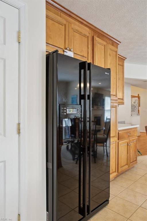 kitchen featuring light tile patterned floors, black fridge with ice dispenser, light countertops, and a textured ceiling