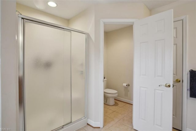 bathroom with tile patterned flooring, toilet, baseboards, and a stall shower