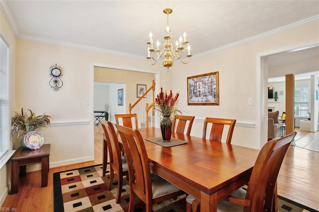 dining area with light wood-type flooring, a fireplace, crown molding, a chandelier, and stairs