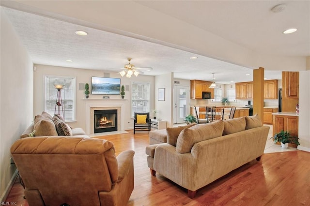 living room featuring baseboards, a fireplace with flush hearth, recessed lighting, light wood-style floors, and a ceiling fan