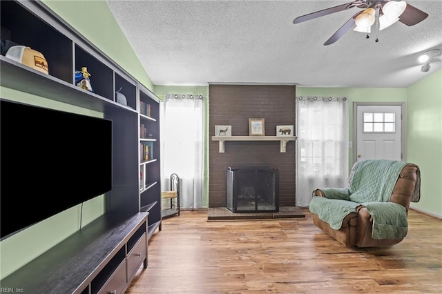 living area with a ceiling fan, wood finished floors, vaulted ceiling, a textured ceiling, and a brick fireplace