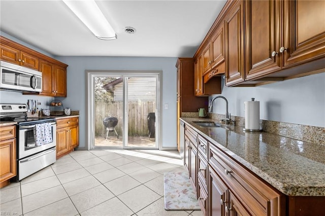 kitchen with dark stone countertops, visible vents, a sink, stainless steel appliances, and brown cabinets