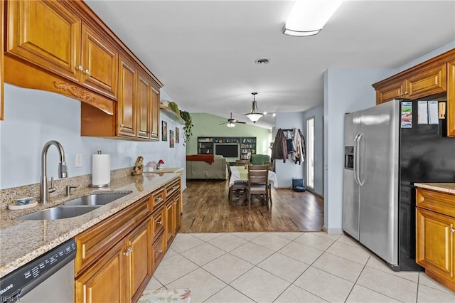 kitchen with light stone countertops, appliances with stainless steel finishes, light tile patterned flooring, brown cabinetry, and a sink