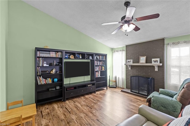 living room featuring wood finished floors, a ceiling fan, a fireplace, vaulted ceiling, and a textured ceiling