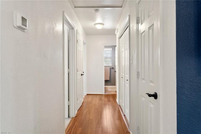 hallway with light wood finished floors, baseboards, and a textured wall