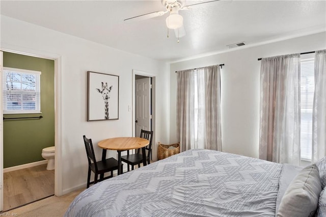 bedroom with visible vents, light carpet, a ceiling fan, ensuite bath, and baseboards