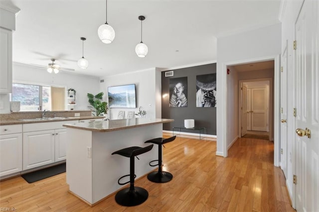 kitchen with a sink, a kitchen breakfast bar, a kitchen island, white cabinets, and light wood finished floors