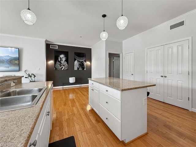 kitchen with visible vents, a kitchen island, light wood-style floors, white cabinetry, and a sink