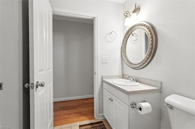 half bath with toilet, vanity, baseboards, and wood finished floors