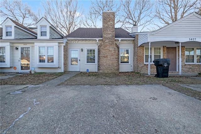 view of front of house featuring brick siding, a chimney, and a shingled roof