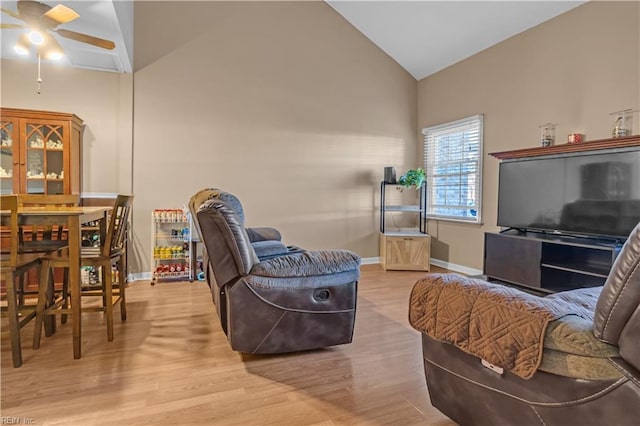 living area featuring baseboards, light wood-style flooring, a ceiling fan, and vaulted ceiling