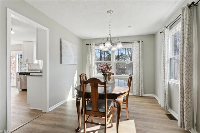 dining room with an inviting chandelier, baseboards, visible vents, and light wood finished floors