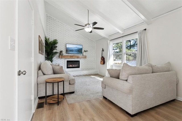 living area with a brick fireplace, ceiling fan, vaulted ceiling with beams, and light wood finished floors