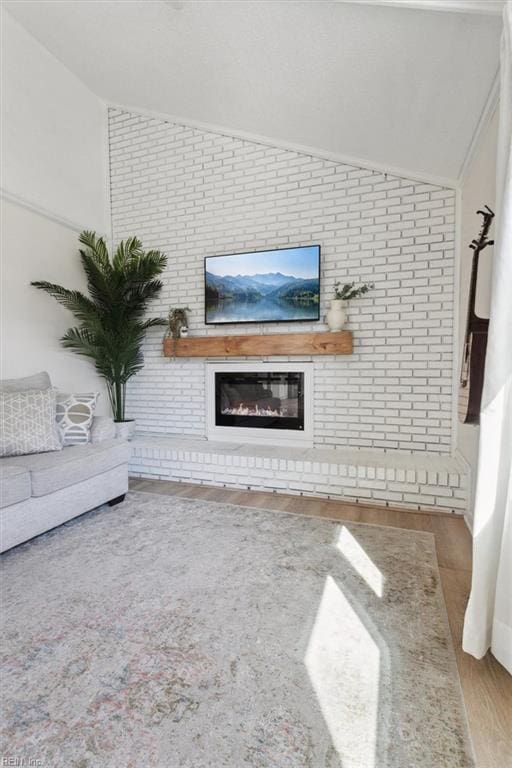 living room with vaulted ceiling, wood finished floors, brick wall, and a large fireplace