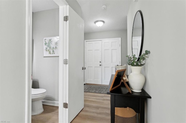 corridor with baseboards, light wood-style floors, and a textured ceiling