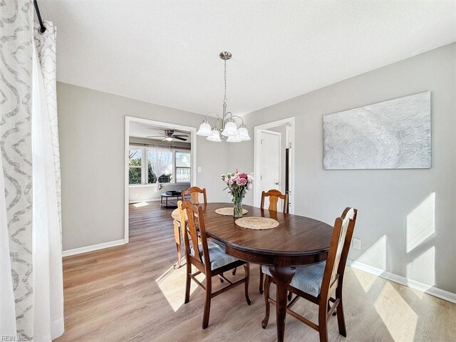 dining area featuring a notable chandelier, light wood-style flooring, a textured ceiling, and baseboards