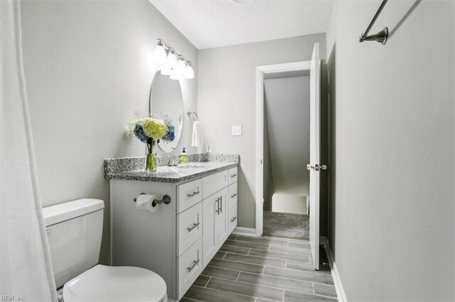 bathroom featuring vanity, baseboards, wood finish floors, a textured ceiling, and toilet