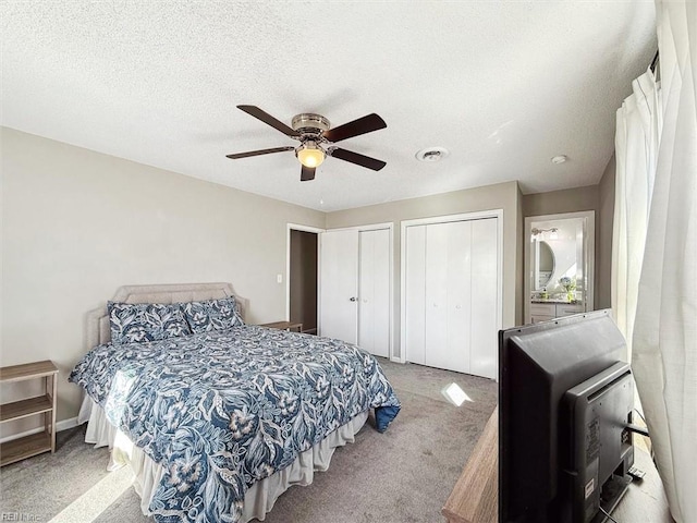 bedroom featuring visible vents, two closets, carpet flooring, a textured ceiling, and a ceiling fan