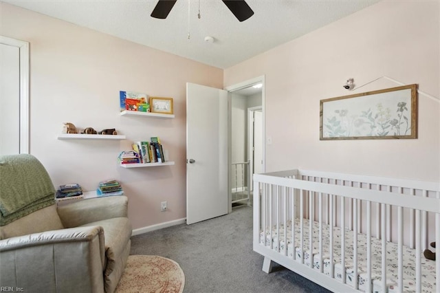 carpeted bedroom featuring baseboards, a nursery area, and ceiling fan