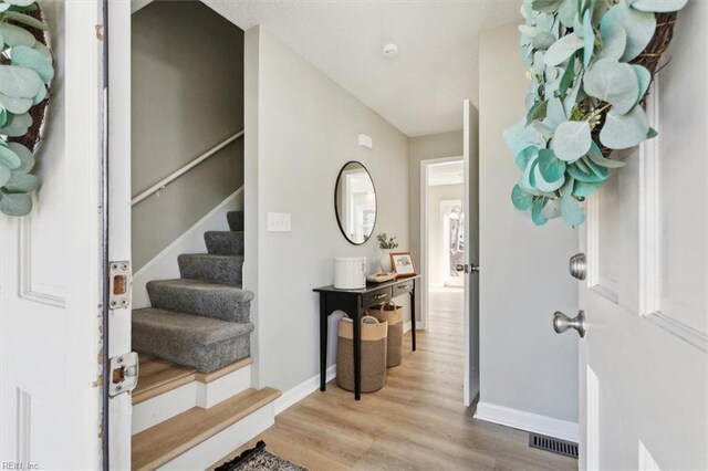 entryway with visible vents, baseboards, light wood-style flooring, and stairway