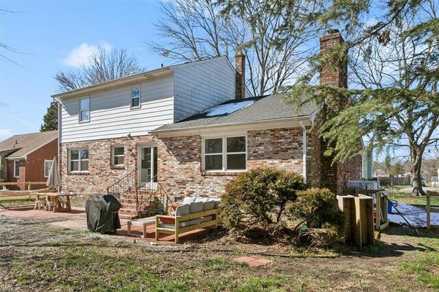 back of property with brick siding, a patio area, a chimney, and a shingled roof