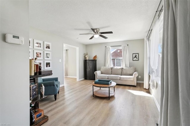 living area featuring ceiling fan, light wood-style floors, baseboards, and a textured ceiling